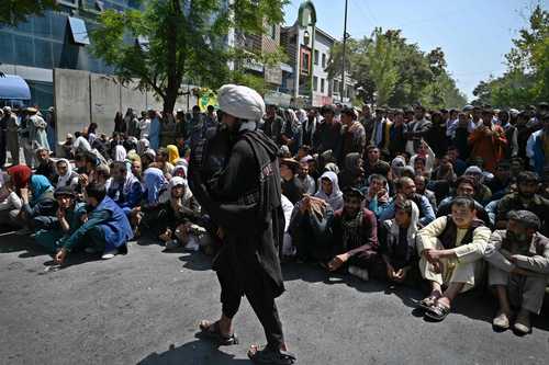  Decenas de personas esperan frente a un banco para retirar efectivo, bajo la vigilancia de un combatiente talibán, en el barrio Shar-e-Naw de Kabul. Foto Afp