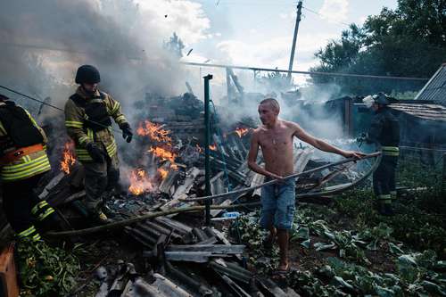 Un residente de la localidad de Bakhmut, en Ucrania, ayuda a los bomberos a sofocar el fuego que destruyó su hogar tras ser blanco de un bombardeo ruso.