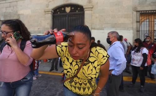 Una mujer se vierte refresco en los ojos para reducir el efecto del gas lacrimógeno arrojado por policías estatales cuando disolvieron una protesta frente al Palacio de gobierno de Oaxaca realizada por habitantes del municipio serrano de Santiago Xiacui.